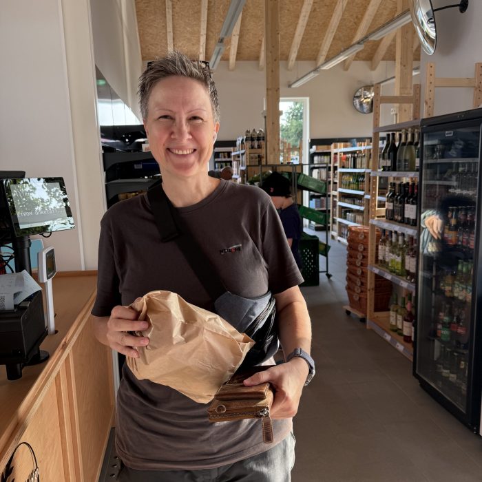 Eine Frau lacht in die Kamere mit einer Brötchentüte in der Hand.