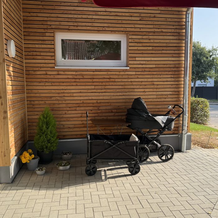 Ein Kinderwagen und ein Bollerwagen stehen vor dem Laden auf der Terasse.