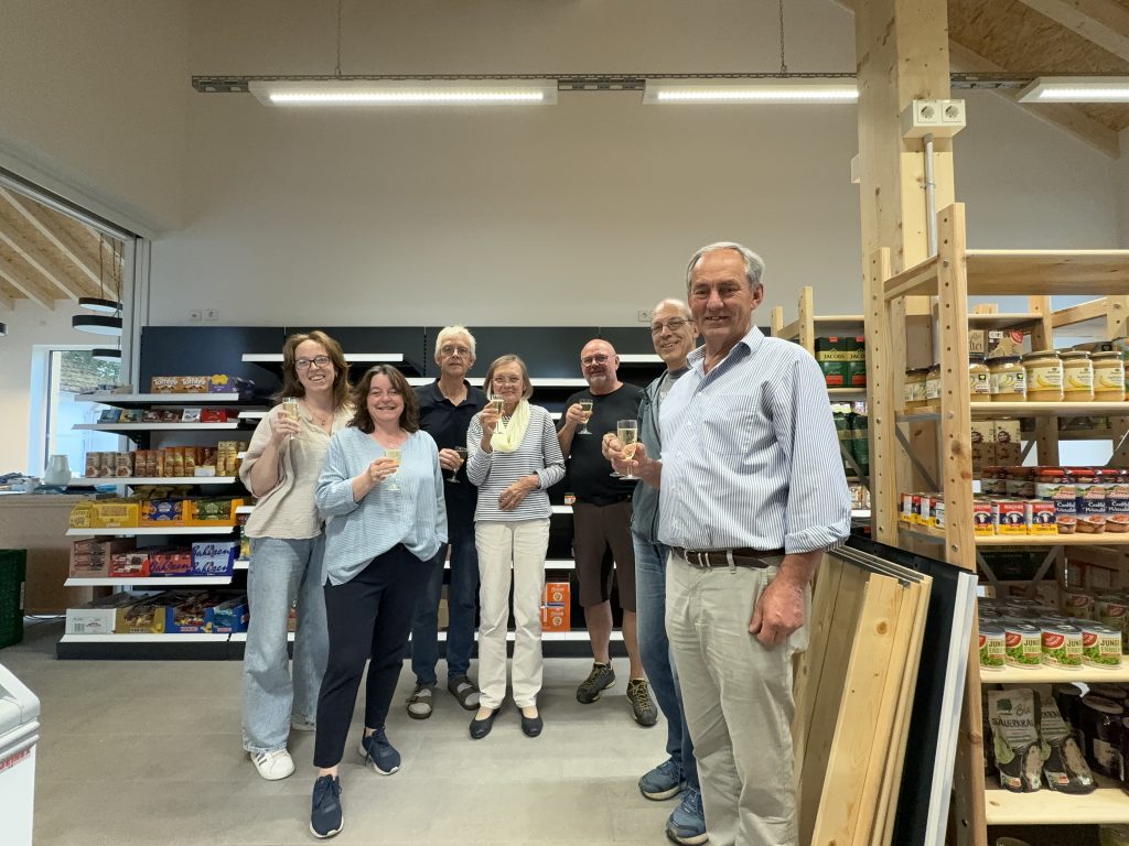 Sieben Menschen stehen für ein Gruppenbild vor den Ladenregalen und halten ein Sektglas in der Hand.