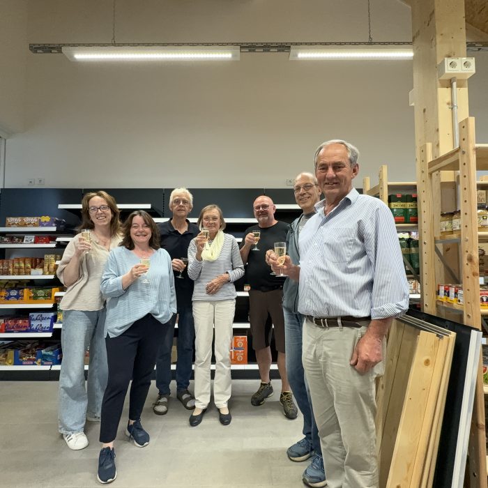 Sieben Menschen stehen für ein Gruppenbild vor den Ladenregalen und halten ein Sektglas in der Hand.